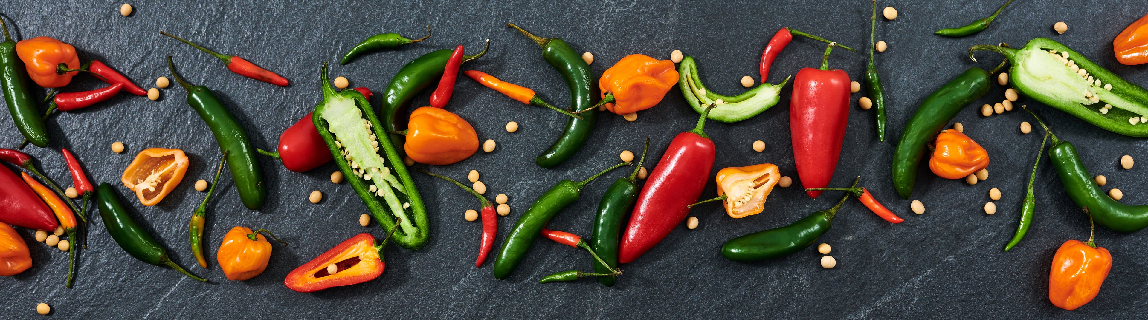 Scattered red, orange, and green hot peppers and soy beans on slate